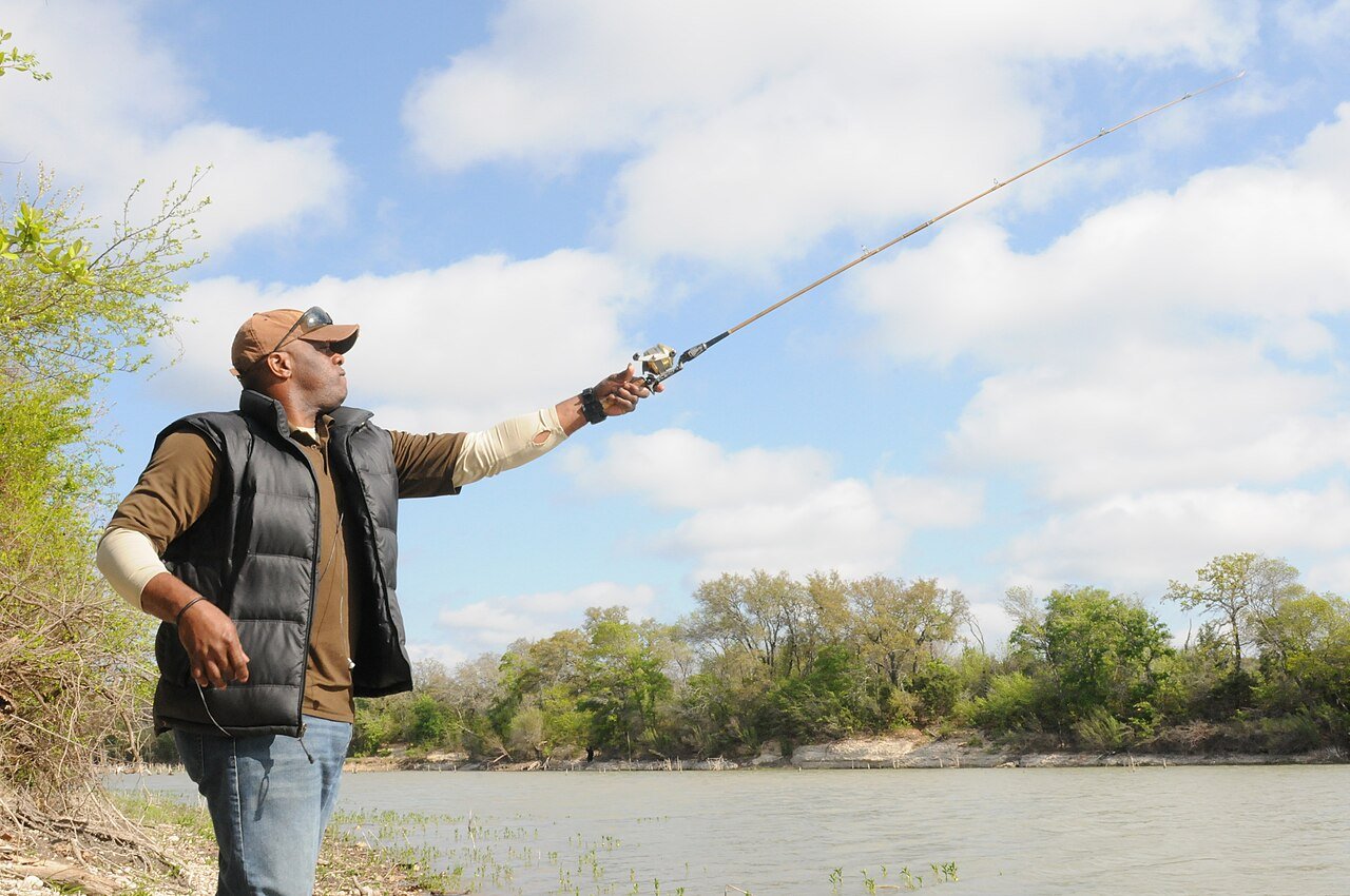 Angler casting a baitcasting rod and reel from a riverbank