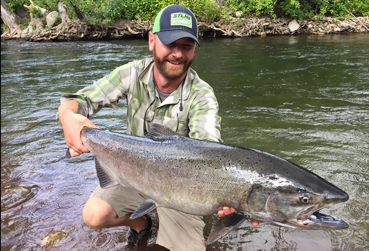 Angler kneeling in a river holding a large chinook salmon
