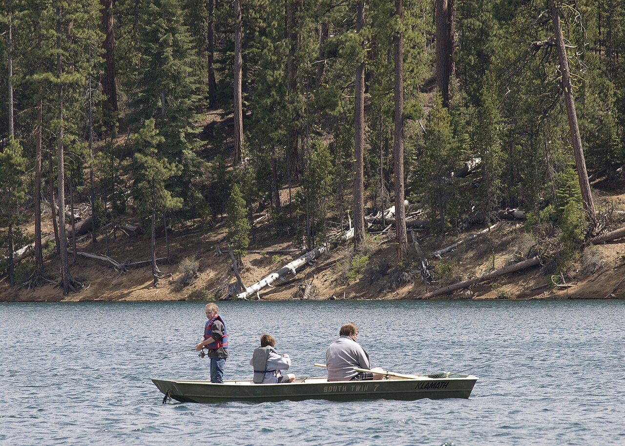 Three anglers fishing from a small aluminum jon boat on a forest lake