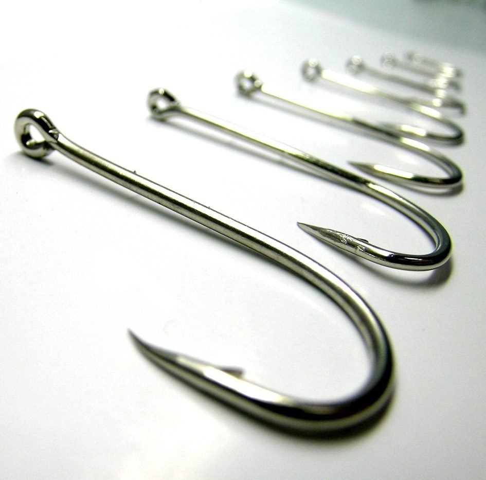 Row of fishing hooks in descending sizes on a white surface