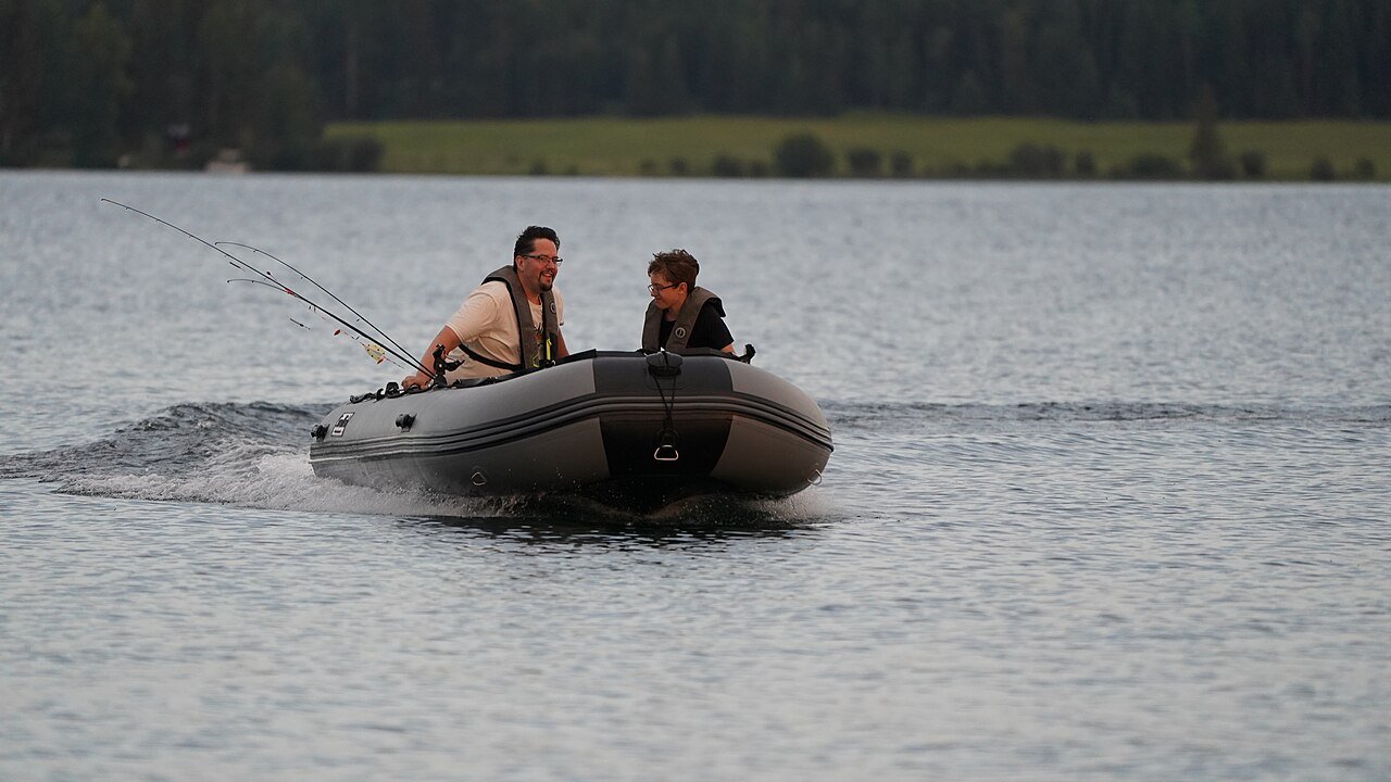 Two anglers in an inflatable fishing boat with rods on a lake